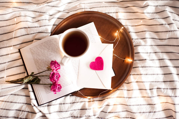 Valentin nap. Egy csésze tea nyitott könyv virágokkal az ágyban. Felülnézet.  - Fotó, kép