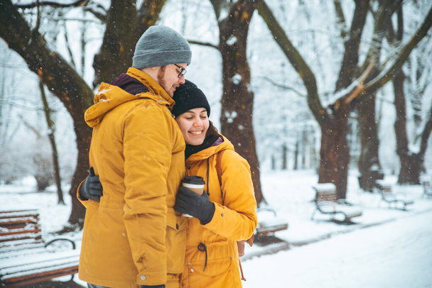 abrazo de pareja en el parque nevado de invierno. beber café para ir a calentar en concepto de día frío
 - Foto, Imagen