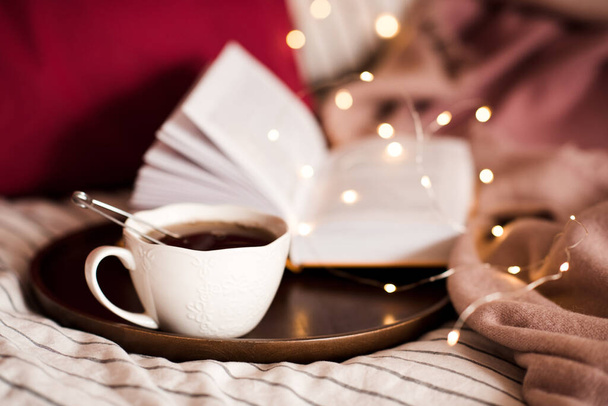 Smaczna czarna herbata w białej filiżance nad otwartą książką ze światłami zbliżenie. Dzień dobry..  - Zdjęcie, obraz