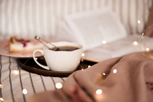 Filiżanka czarnej herbaty nad otwartą książką i światła w tle w łóżku zbliżenie. - Dzień dobry. Śniadanie.  - Zdjęcie, obraz