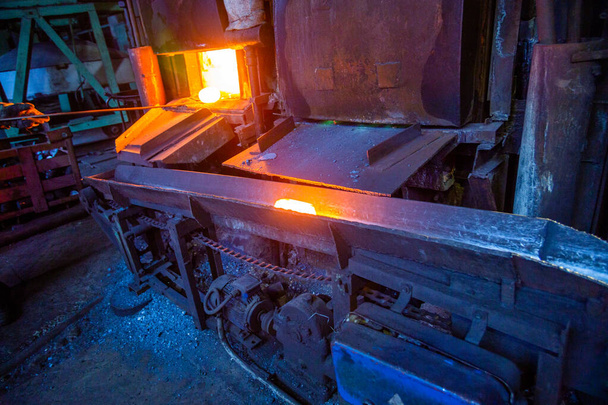 Ein Prozess der Bewegung von glühend heißen Stahlwerkstücken vom Ofen zum Hammer mit Kettenförderer. - Foto, Bild