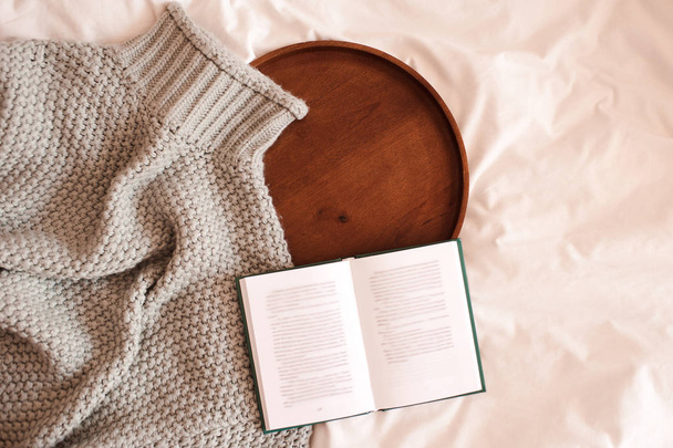 Pull tricoté avec livre opn et plateau en bois au lit sur gros plan blanc. Vue de dessus. Concept de saison hivernale
.  - Photo, image