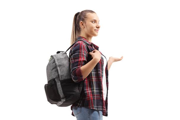 Full length profile shot of a teenage female student standing and gesturing with her hand isolated on white background - Foto, afbeelding