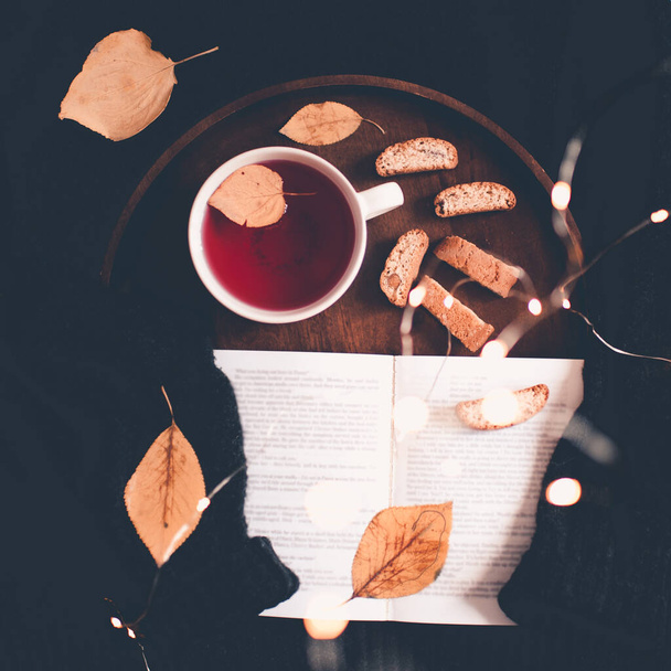 Egy csésze tea lehullott levelekkel és nyitott könyv marad kötött pulóver közelkép. Első látásra. Jó reggelt..  - Fotó, kép
