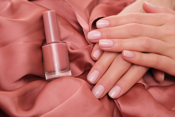 Beautiful female hands with delicate,natural manicure lying on satin. Beautiful light salmon- pink color. - Photo, Image