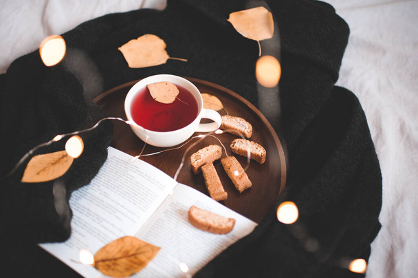 Őszi csésze vörös tea lehullott levelekkel és nyitott könyv kötött pulóverről az ágyban. - Jó reggelt! Őszi szezon. Reggeli.  - Fotó, kép