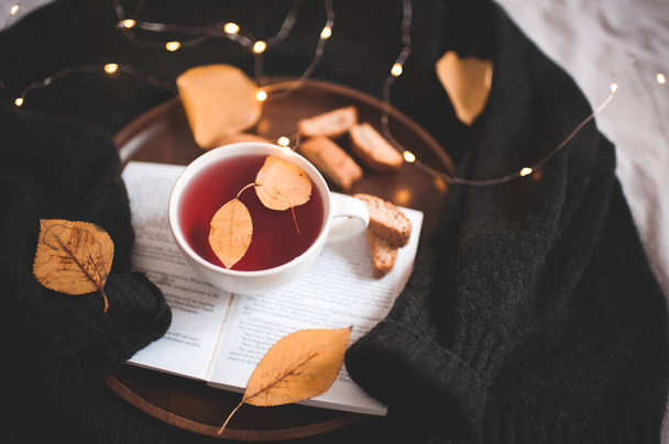 Aranyos csésze tea lehullott levelekkel, nyitott könyv közelről, ragyogó fények felett. - Jó reggelt! Reggeli.   - Fotó, kép