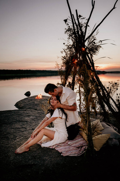 Young couple is embracing and kissing in wigwam on the coast. Romantic love story. Idea for photosession. - Foto, imagen