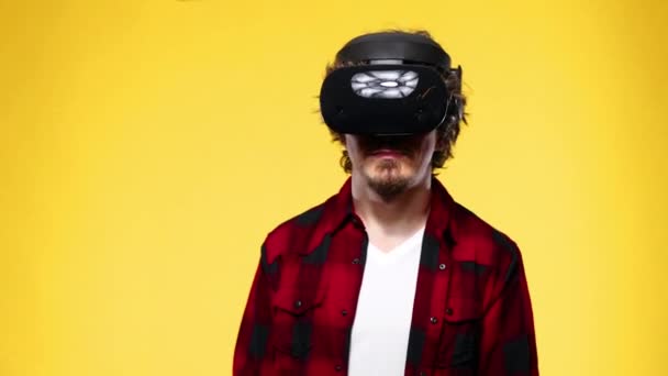 Young man with curly hair using a VR headset and experiencing virtual reality isolated on yellow background - 映像、動画