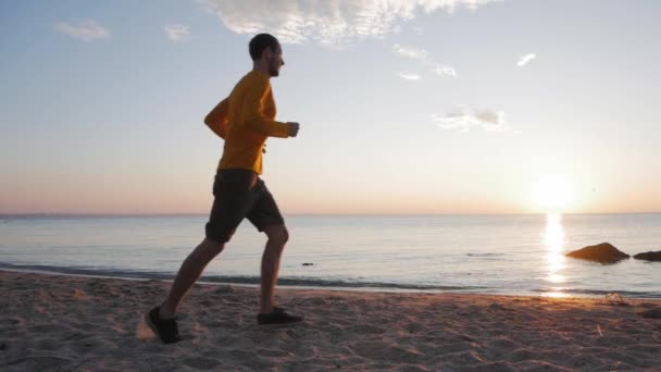 Sabahları güneşli plajda genç erkek koşucu eğitimi. - Video, Çekim