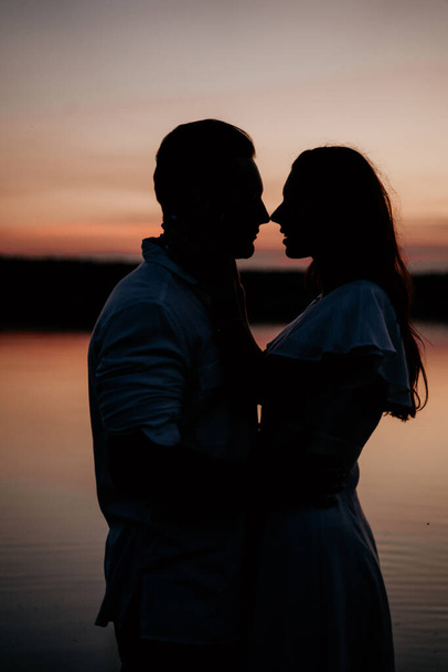 Young couple embracing and kissing in the water on Sunset. Two silhouettes against the sun. Romantic love story. - Photo, image