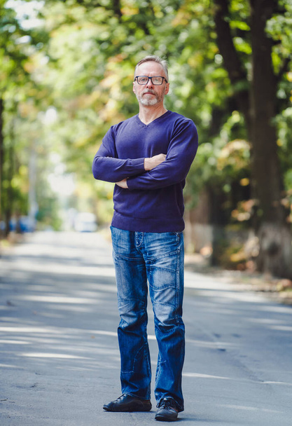 Man with gray hair outdoor in park. No jacket. Blue sweater. Eyeglasses. Bearded confident businessman. Blurred background. - Valokuva, kuva
