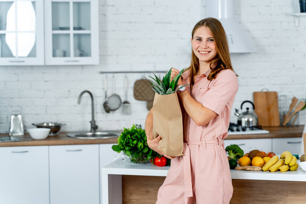 woman with the grocery store packet in the hands. Kitchen background. Young woman with healthy food. - Fotoğraf, Görsel