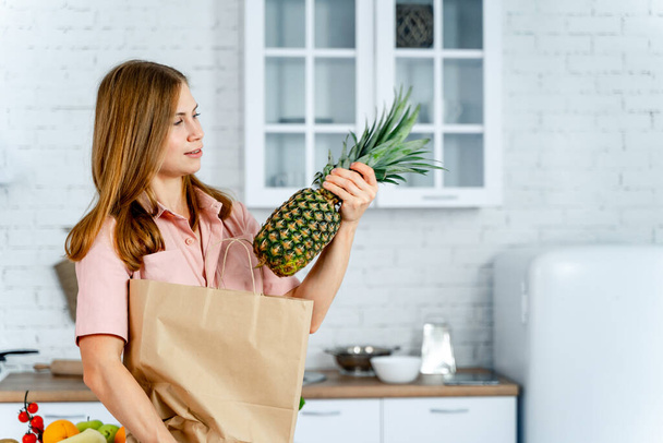 woman with the grocery store packet in the hands. Kitchen background. Young woman with healthy food. Pineapple in hands - Foto, immagini