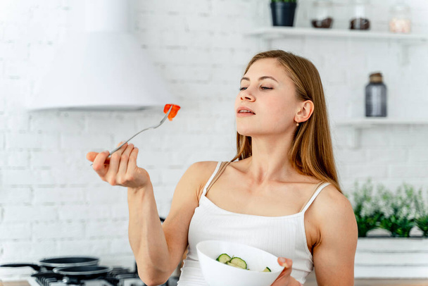 Mulher atraente cheiro de tomate cortado em garfo na cozinha moderna. Fundo desfocado. Alimentação saudável e conceito de estilo de vida. Fechar.
. - Foto, Imagem