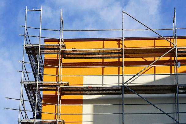 ремонт фасада дома и теплоизоляция, леса, синий фон неба
 - Фото, изображение