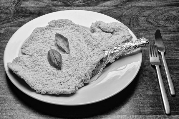 Еда; сырой хлеб Милан котлет стейк с листьями базилика на белом блюде
 - Фото, изображение