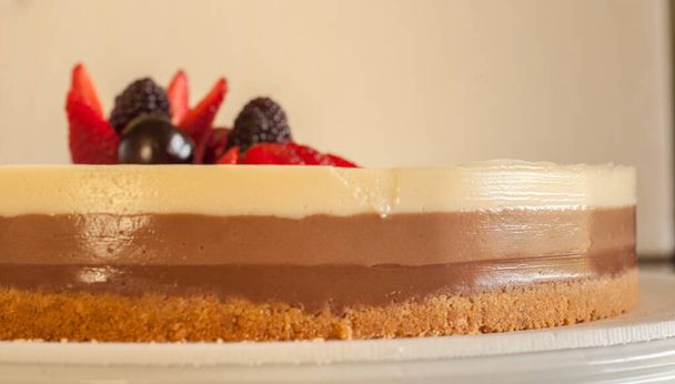 gâteau de trois chocolats différents avec biscuit croquant base de biscuit et garni de cerises aux fraises et fraises sur une assiette blanche
 - Photo, image