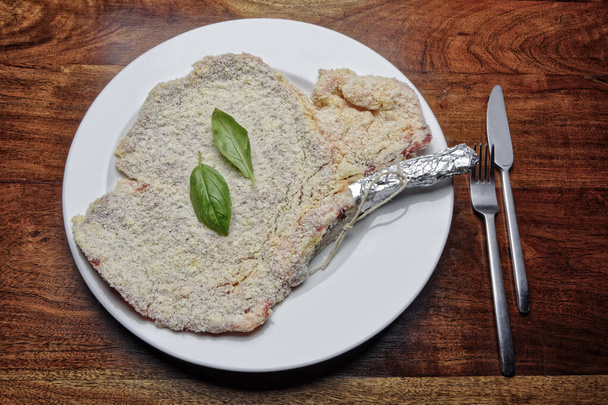 Еда; сырой хлеб Милан котлет стейк с листьями базилика на белом блюде
 - Фото, изображение