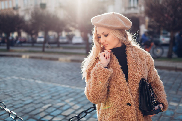 Spring fashionable female accessories. Stylish woman wearing teddy coat beret and holding purse in city outdoors. Clothes and trendy outfit - Photo, Image
