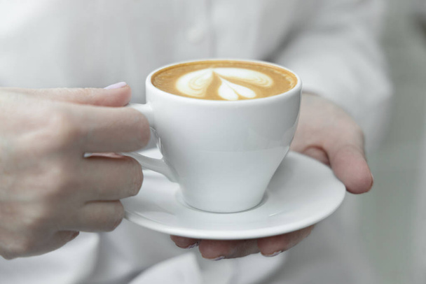 Woman hands holding cup of hot coffee latte cappuccino with with lush milk foam heart shaped. - Photo, Image