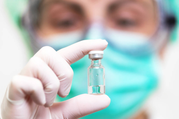 Γιατρός με ιατρικά γάντια και μάσκα που κρατάει αμπούλα με εμβόλιο. Κοντινό πλάνο. Coronavirus, επιδημία και ιατρική έννοια. - Φωτογραφία, εικόνα
