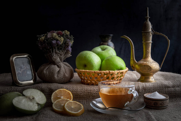 Naturaleza muerta, té de la mañana con limones y manzanas en un ambiente hogareño, en colores oscuros con iluminación brillante
. - Foto, Imagen