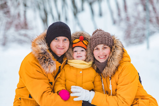 portret młodej uśmiechniętej rodziny na żółtych płaszczach zimowych patrzących w kamerę. matka ojciec i mała córka - Zdjęcie, obraz
