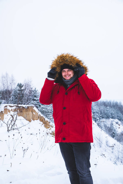 smiling young man in red winter coat with fur hood snowed field on background. - Photo, image