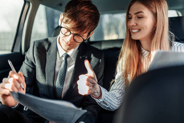Image of a young businessman, a man and a woman in official clothes, sitting in a car with working documents - Foto, Imagen