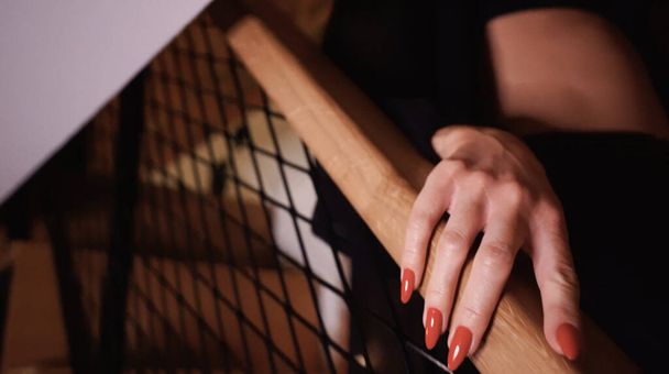 beautiful female fingers with delicate red nails closeup. Holding stair railings. Black lingerie out of focus. - Фото, изображение