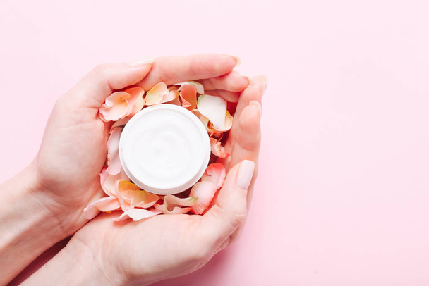 Vaso aperto con crema per la cura della pelle e petali di rose in mani femminili su sfondo rosa
. - Foto, immagini