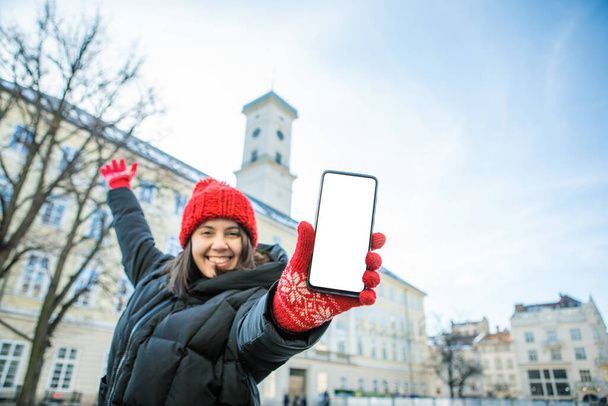 Kırmızı şapkalı adam elinde beyaz boş ekran Avrupa belediye binası arka plan seyahat konseptiyle telefon tutuyor. - Fotoğraf, Görsel