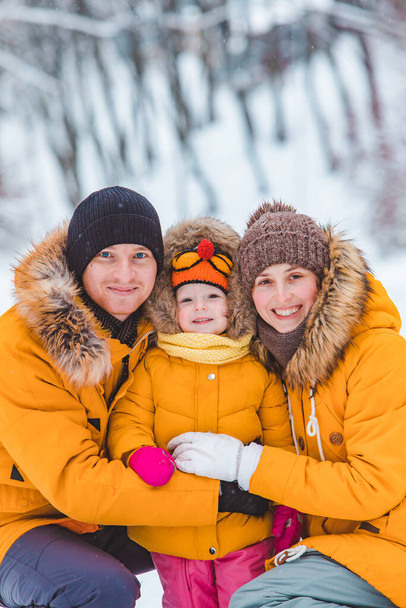 portret van jonge glimlachende familie bij gele winterjassen die naar de camera kijken. moeder vader en dochtertje - Foto, afbeelding