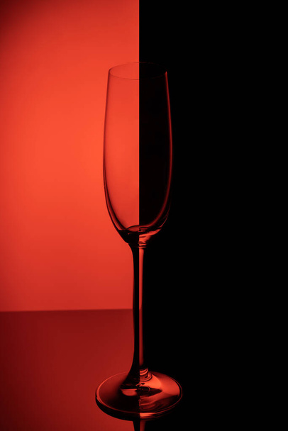 Copo de champanhe vazio com reflexão, sobre fundo gradiente vermelho e preto. Conceito de vida clube
. - Foto, Imagem