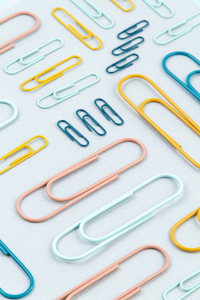 Top view of Colorful paper clips over the  pastel background. Modern abstract concept of working space, studies, office desk - Photo, Image