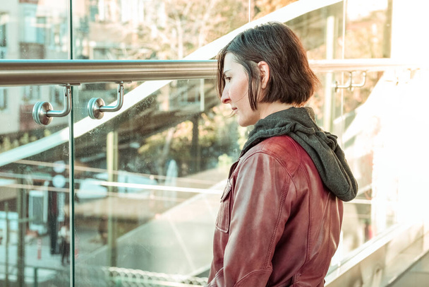 Mujer morena con chaqueta de cuero rojo mirando a través de la ventana de una estación de tren. Concepto de expectativa
. - Foto, imagen