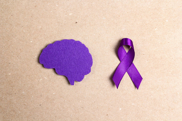 Purple awareness ribbon and brain symbol on a brown background. Epilepsy disease or Alzheimer disease awareness world day. - 写真・画像