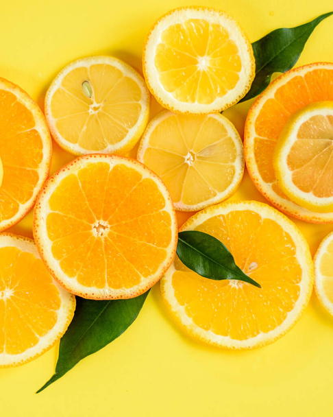 Vlakke lay van gesneden sinaasappelen en citroenen op een gele achtergrond - Foto, afbeelding