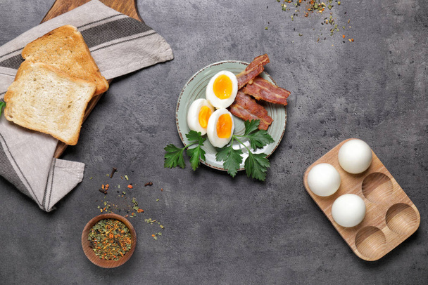 Teller mit gekochten Eiern, Speck und Toastbrot auf dunklem Hintergrund - Foto, Bild