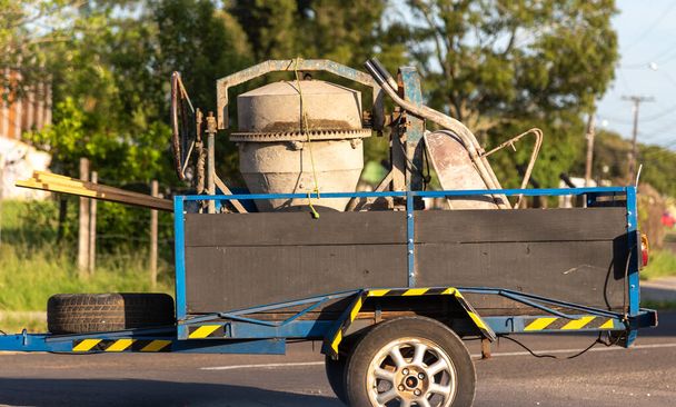 A concrete mixer used to make cement and concrete being transported in a blue trailer pulled by a passenger car. Equipment used in engineering and construction works. transport. - Photo, Image