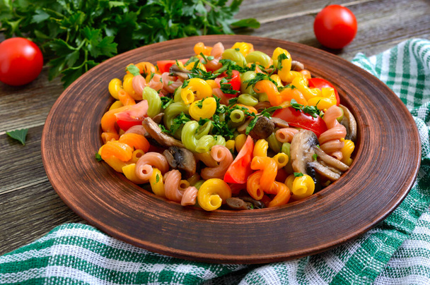Вкусный тёплый салат. Цветная паста с грибами и свежими помидорами в миске на деревянном столе. Pasta colorata
. - Фото, изображение