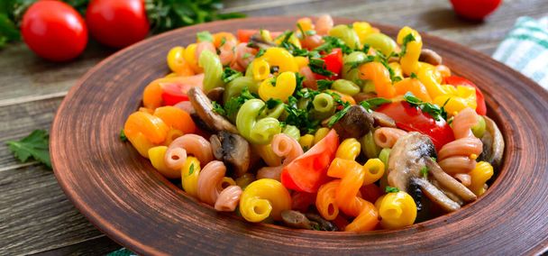 Tasty warm salad. Colored pasta with mushrooms and fresh tomatoes in a bowl on a wooden table. Pasta colorata. - Photo, Image