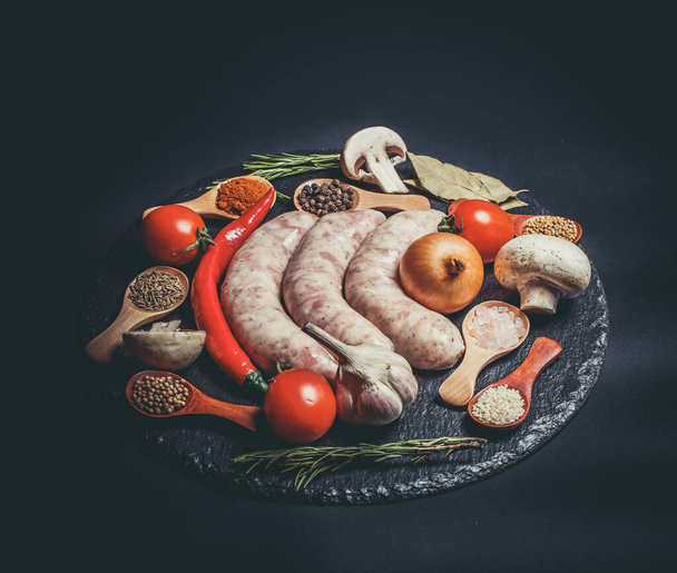 Raw sausages, different vegetables, spices and ingredients on a black background - Φωτογραφία, εικόνα