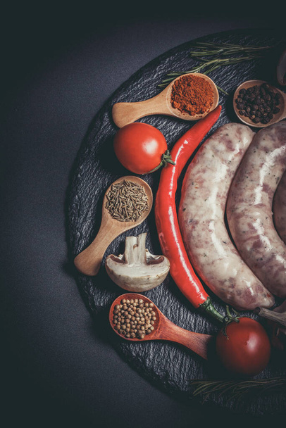 Raw sausages, different vegetables, spices and ingredients on a black background - Fotó, kép