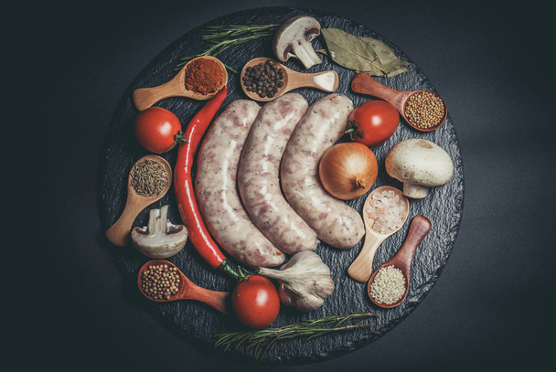 Raw sausages, different vegetables, spices and ingredients on a black background - Fotoğraf, Görsel