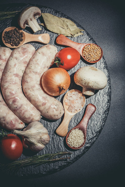 Raw sausages, different vegetables, spices and ingredients on a black background - Foto, afbeelding