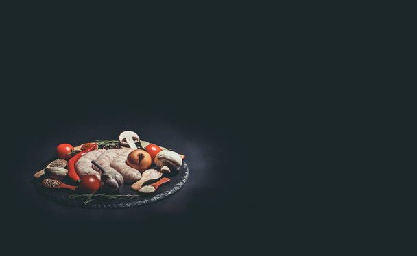 Raw sausages, different vegetables, spices and ingredients on a black background - 写真・画像
