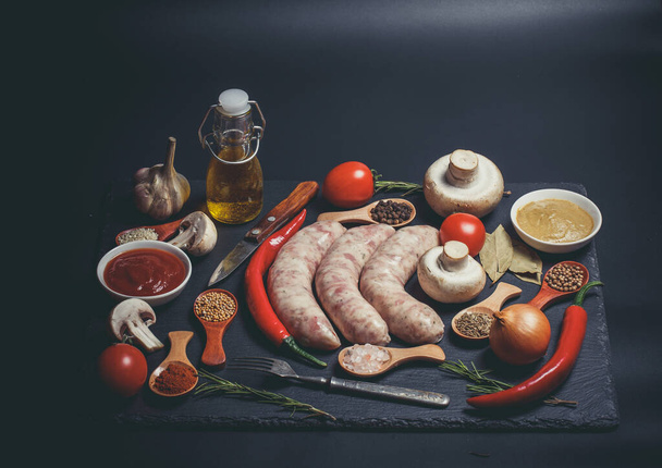 Raw sausages, different vegetables, spices and ingredients on a black background - Photo, Image