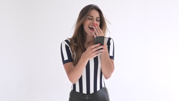 Cheerful pretty cheerleader woman laughing and covering her mouth while using smartphone over grey background - Imágenes, Vídeo